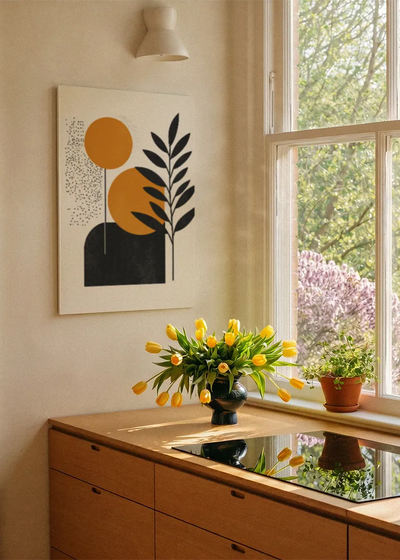 Akustikbillede med orange cirkler med et sort blad, ved et vindue med en blomsterbuket i karmen