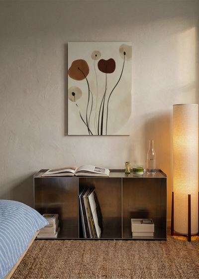 Akustikbillede med brune blomster på lange stilke, over sengegavlen i et soveværelse med tændt lampe