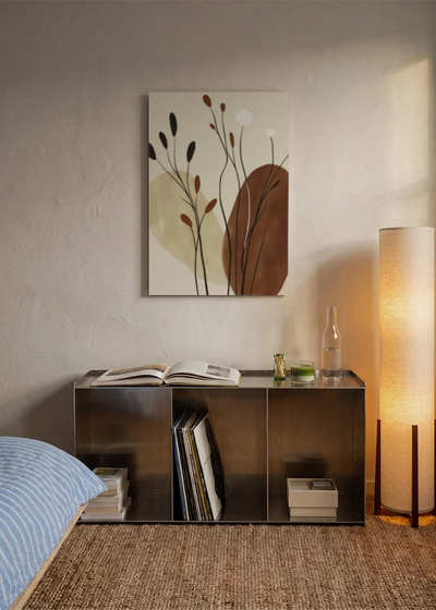 Akustikbillede med brune blade og grene i beige toner, over sengegavlen i et soveværelse med tændt lampe