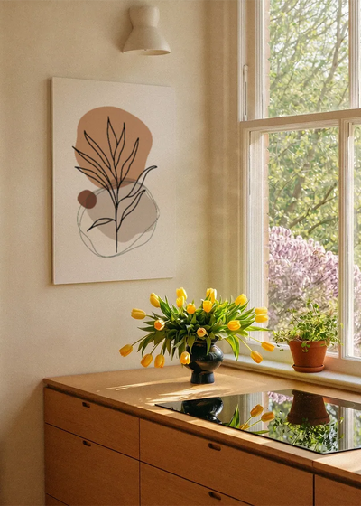 Akustikbillede med et terrakottafarvet blad med organiske former, ved et vindue med en blomsterbuket i karmen