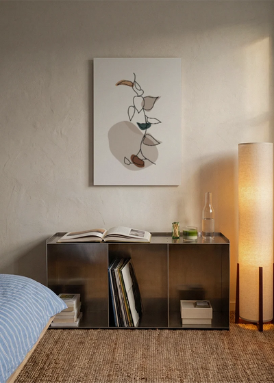 Akustikbillede med hvide blomster med brune former, over sengegavlen i et soveværelse med tændt lampe