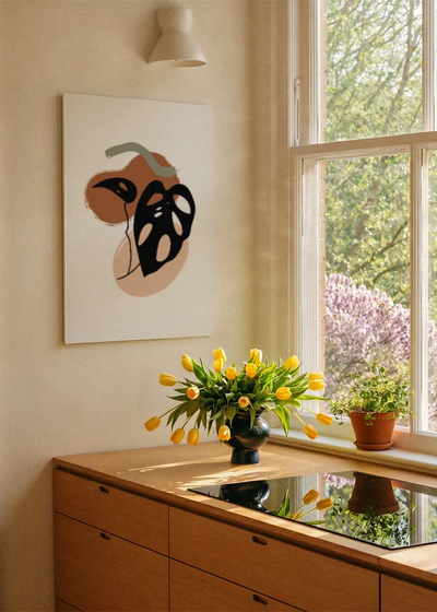Akustikbillede med et sort monsterablad med orange former, ved et vindue med en blomsterbuket i karmen
