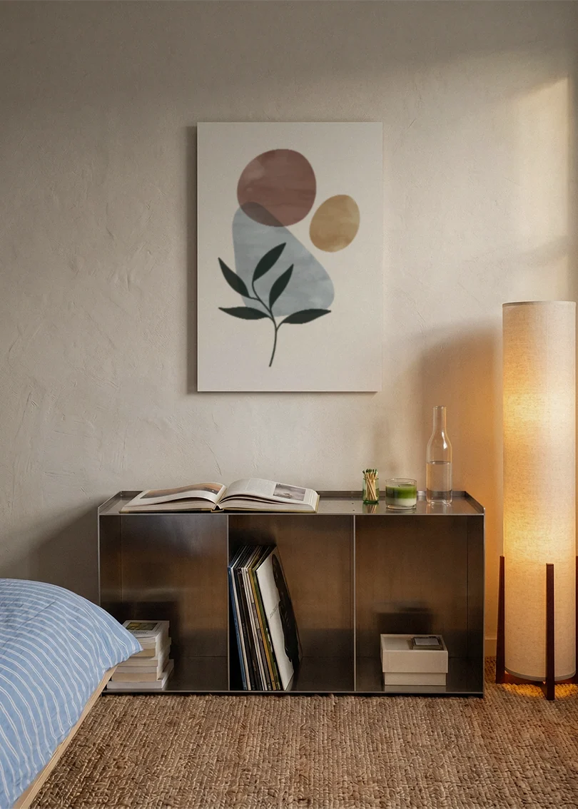 Akustikbillede med et grønt blad med grå og gyldne cirkler, over sengegavlen i et soveværelse med tændt lampe