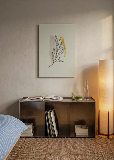 Akustikbillede med et gult blad med tegnede konturer, over sengegavlen i et soveværelse med tændt lampe