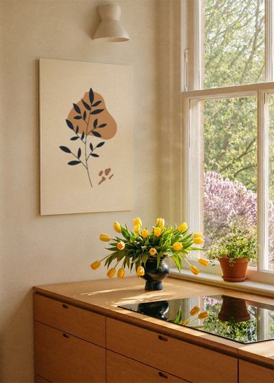 Akustikbillede med sorte blade på en orange form, ved et vindue med en blomsterbuket i karmen