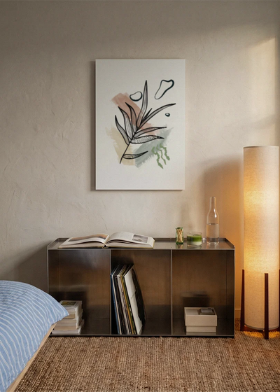 Akustikbillede med tegnede grene med lyserøde former, over sengegavlen i et soveværelse med tændt lampe