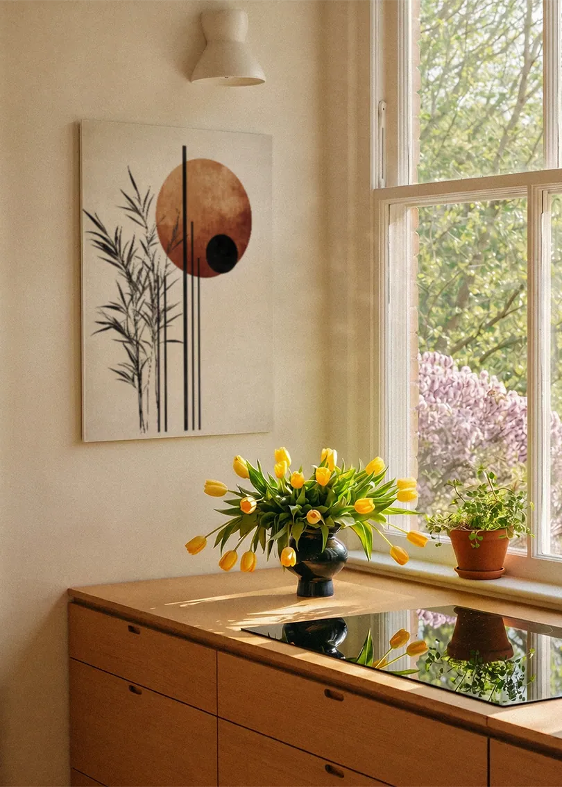 Akustikbillede med sorte grene og en terrakottafarvet cirkel, ved et vindue med en blomsterbuket i karmen
