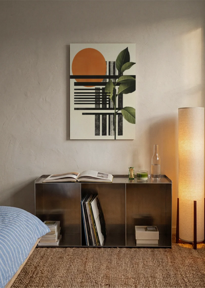 Akustikbillede med en orange cirkel med sorte striber og grønne blade, over sengegavlen i et soveværelse med tændt lampe