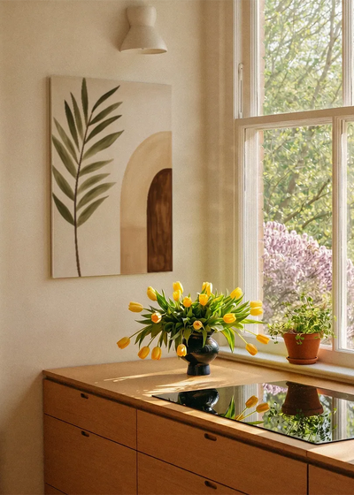 Akustikbillede med et grønt palmeblad ved en brun bue, ved et vindue med en blomsterbuket i karmen