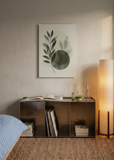 Akustikbillede med grønne blade i overlappende cirkler, over sengegavlen i et soveværelse med tændt lampe