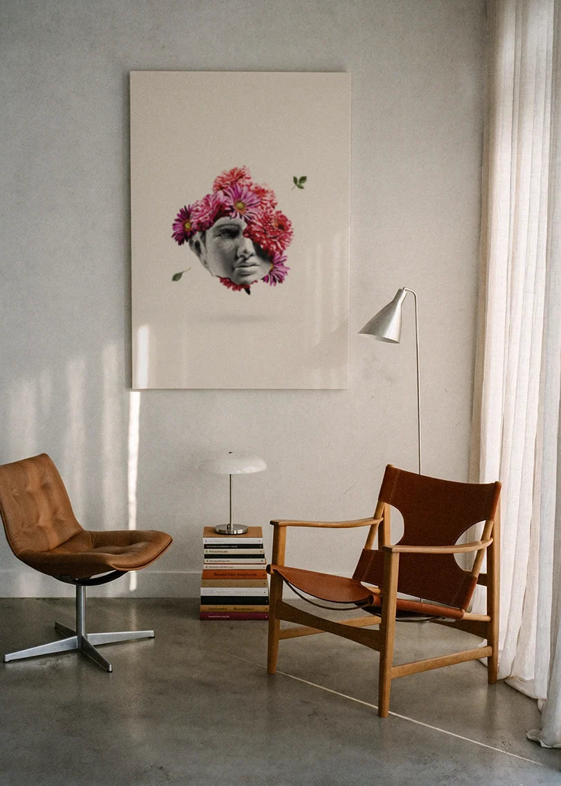 Akustikbillede med en gipsbuste der opløses i blomster, ophængt over en lænestol ved gardinet med gulvlampe