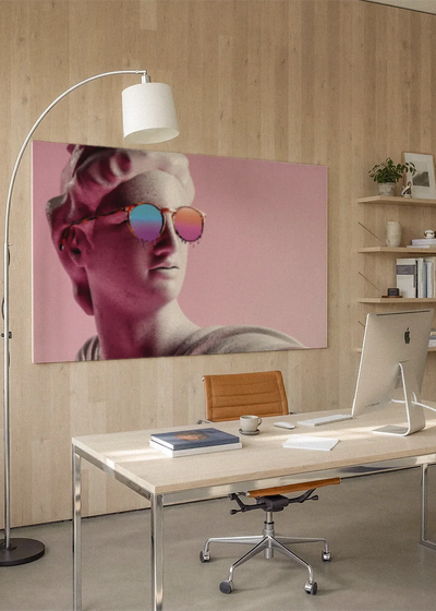 Akustikbillede med en gipsbuste med solbriller på pink baggrund, på et hjemmekontor med hvidt skrivebord og buelampe