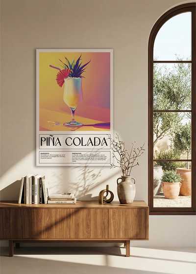 Akustikbillede med en retro cocktailplakat med Pina Colada, over en skænk i valnød ved et buet vindue