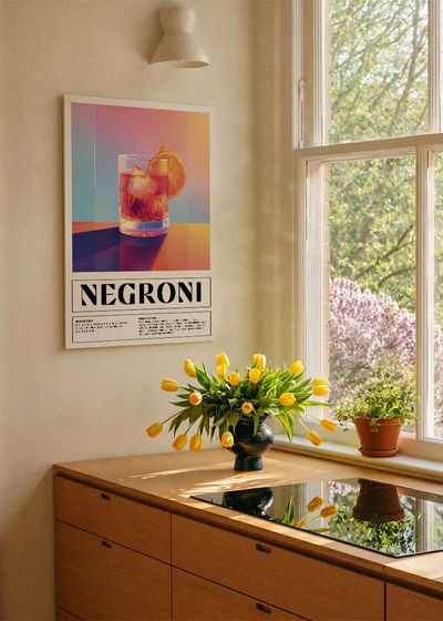 Akustikbillede med en retro cocktailplakat med Negroni, ved et køkkenvindue med gule tulipaner