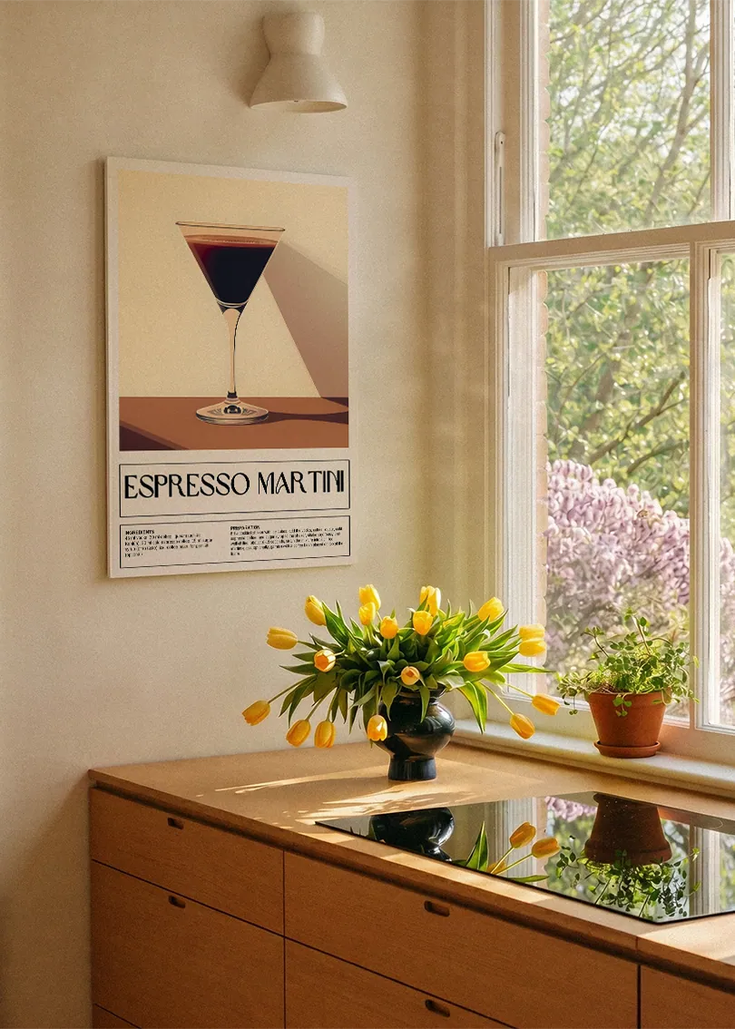 Akustikbillede med en retro cocktailplakat med Espresso Martini, ved et køkkenvindue med gule tulipaner