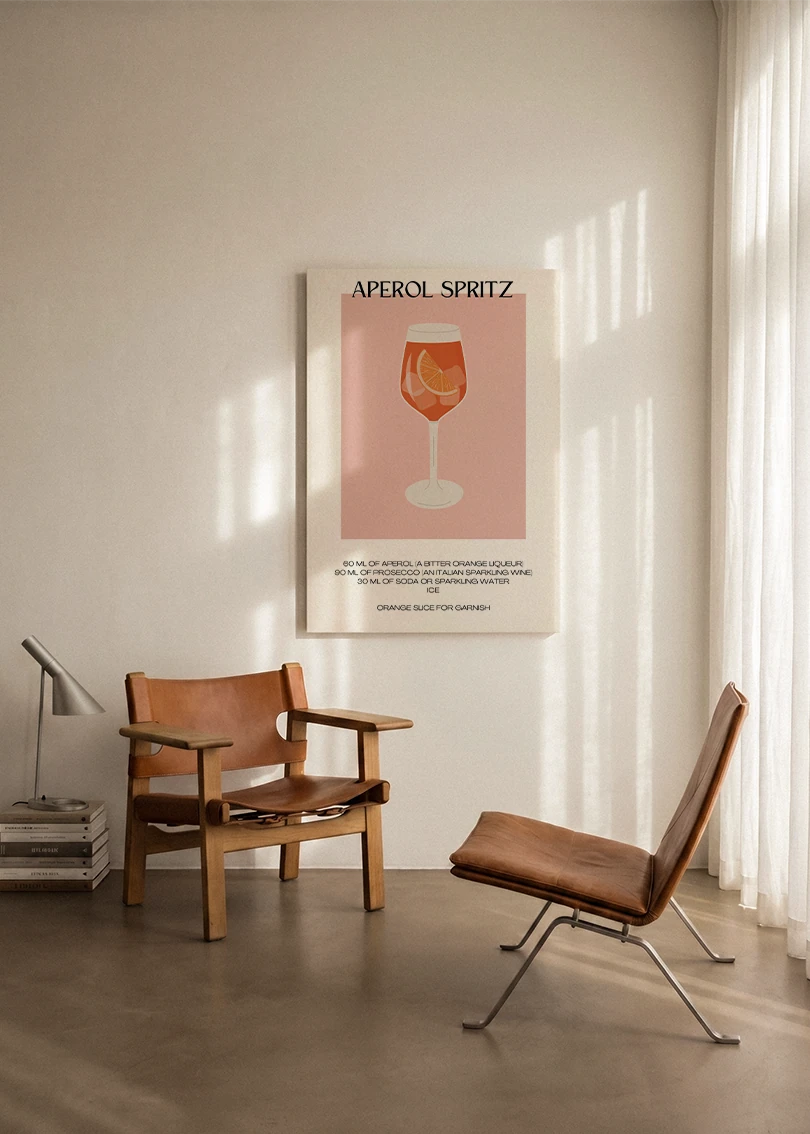 Akustikbillede med en minimalistisk cocktailplakat med Aperol Spritz, ophængt over en lænestol ved gardinet