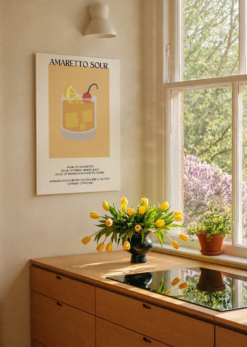 Akustikbillede med en minimalistisk cocktailplakat med Amaretto Sour, ved et køkkenvindue med gule tulipaner