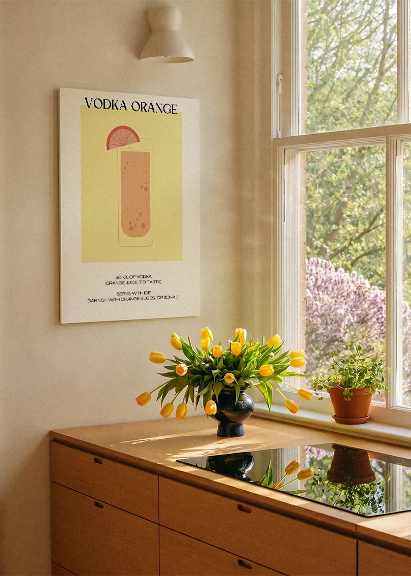 Akustikbillede med en minimalistisk cocktailplakat med Vodka Orange, ved et køkkenvindue med gule tulipaner