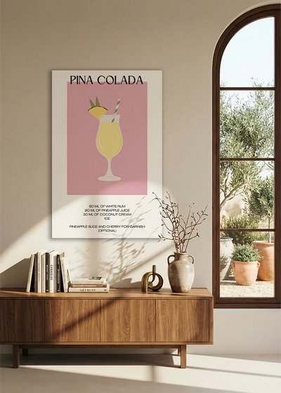 Akustikbillede med en minimalistisk cocktailplakat med Pina Colada, over en skænk i valnød ved et buet vindue