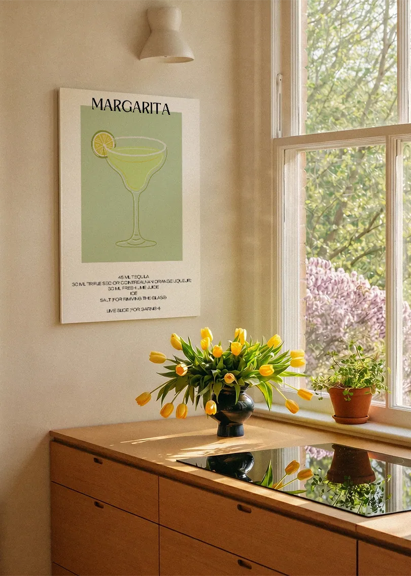 Akustikbillede med en minimalistisk cocktailplakat med Margarita, ved et køkkenvindue med gule tulipaner