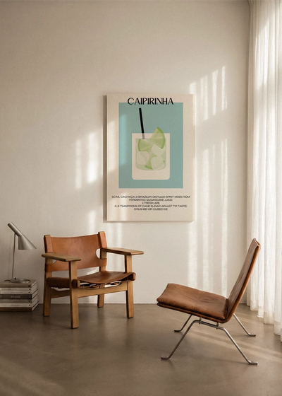 Akustikbillede med en minimalistisk cocktailplakat med Caipirinha, ophængt over en lænestol ved gardinet