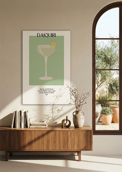Akustikbillede med en minimalistisk cocktailplakat med Daiquiri, over en skænk i valnød ved et buet vindue