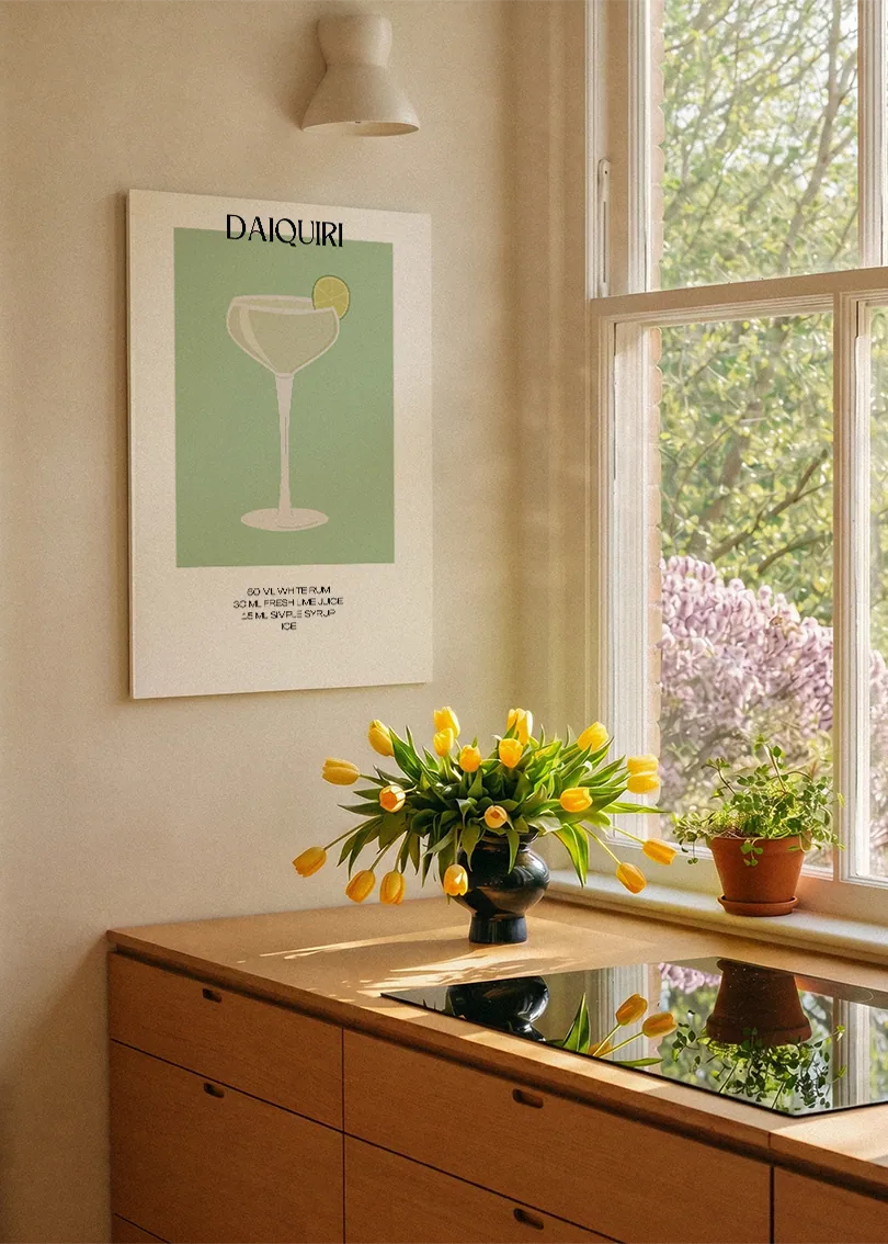 Akustikbillede med en minimalistisk cocktailplakat med Daiquiri, ved et køkkenvindue med gule tulipaner