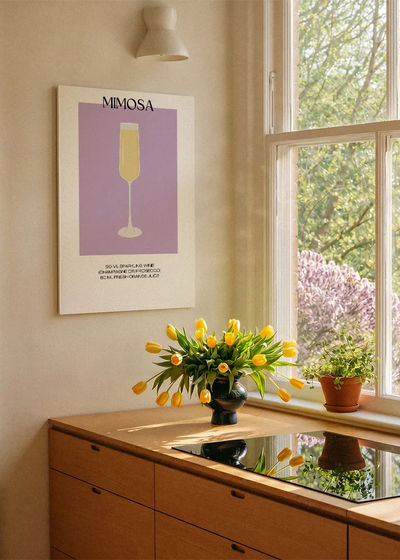 Akustikbillede med en minimalistisk cocktailplakat med Mimosa, ved et køkkenvindue med gule tulipaner