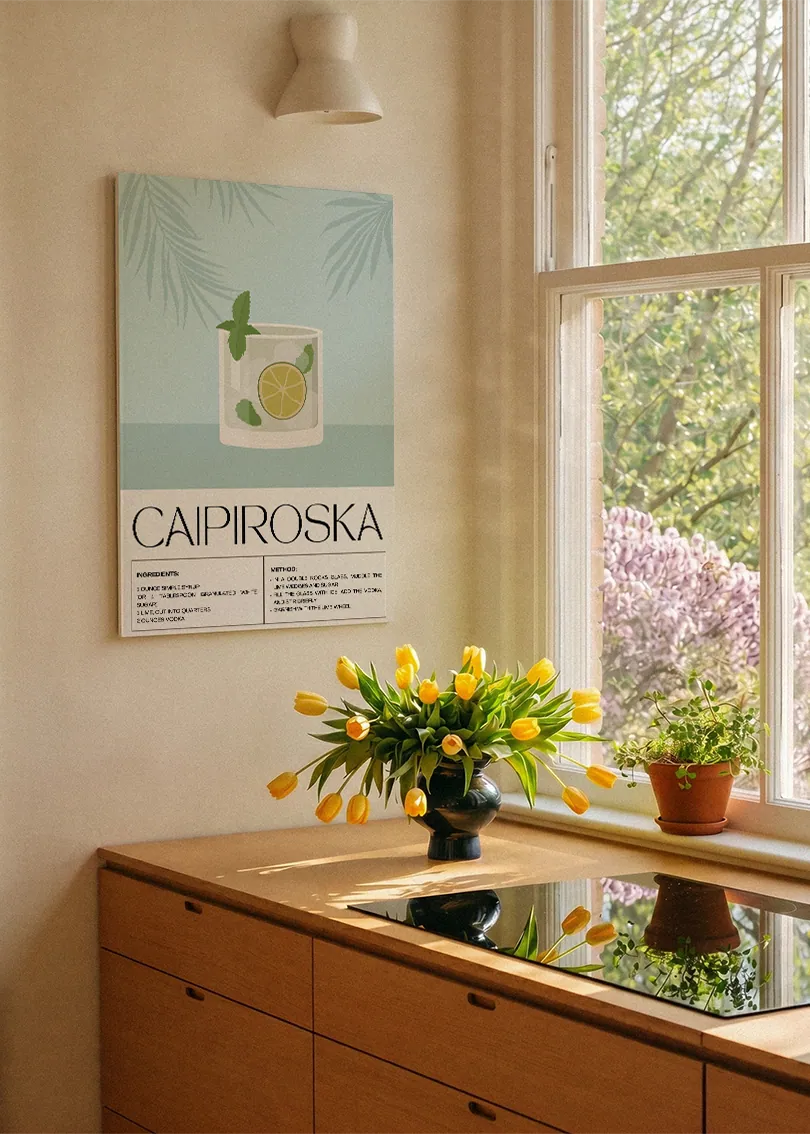 Akustikbillede med en retro cocktailplakat med Caipiroska, ved et køkkenvindue med gule tulipaner