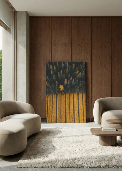 Akustikbillede med dronefoto af mørk nåleskov mod stribede gule marker, i lounge med bugtet sofa mod vægpanel i valnød