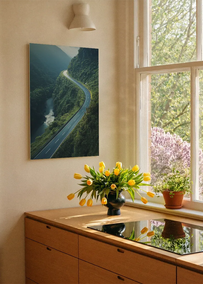 Akustikbillede med dronefoto af en snoet bjergvej langs en flod i en grøn dal, i køkken ved vindue med gule tulipaner