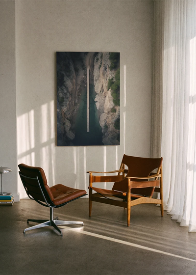 Akustikbillede med dronefoto af en vej gennem en dyb klippekløft, ophængt i stue med brune lædestole