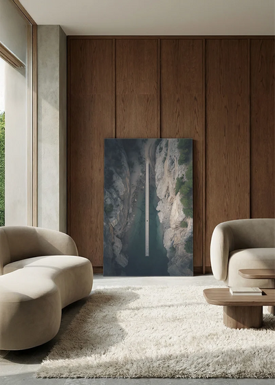 Akustikbillede med dronefoto af en vej gennem en dyb klippekløft, i lounge med bugtet sofa mod vægpanel i valnød