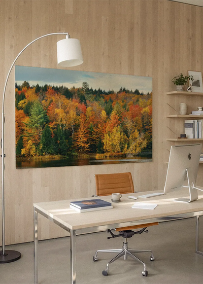 Akustikbillede med efterårsskov i orange, rødt og gult ved en skovsø, på hjemmekontor med hvidt skrivebord og buelampe