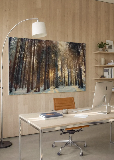 Akustikbillede med sneklædt nåleskov med lavtstående sol, på hjemmekontor med hvidt skrivebord og buelampe