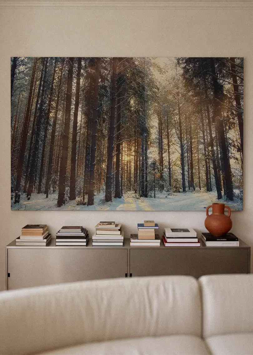 Akustikbillede med sneklædt nåleskov med lavtstående sol, over sofa med bøger og terrakottavase