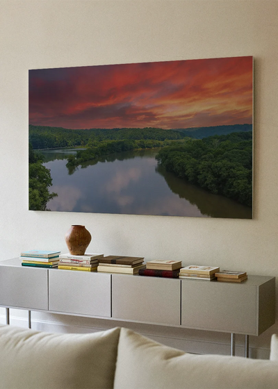 Akustikbillede med en flod ved solnedgang under rød og orange himmel, over hvid skænk med sofa i forgrunden