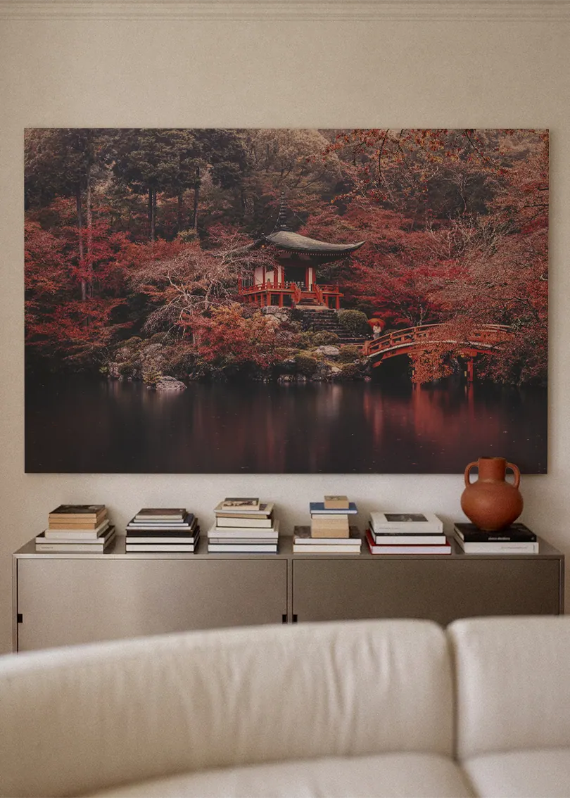 Akustikbillede med et japansk tempel i rød efterårsskov ved vand, over sofa med bøger og terrakottavase